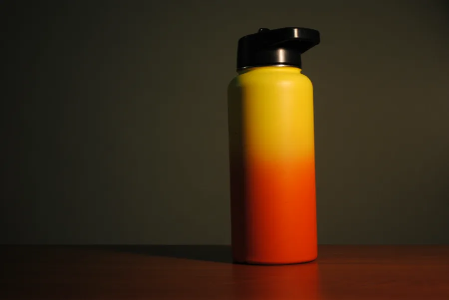 Product photo of a yellow and orange water bottle on a wooden table.