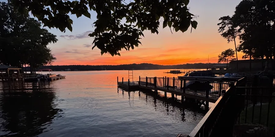 Sunset over a lake, seen from a dock with a black railing.
